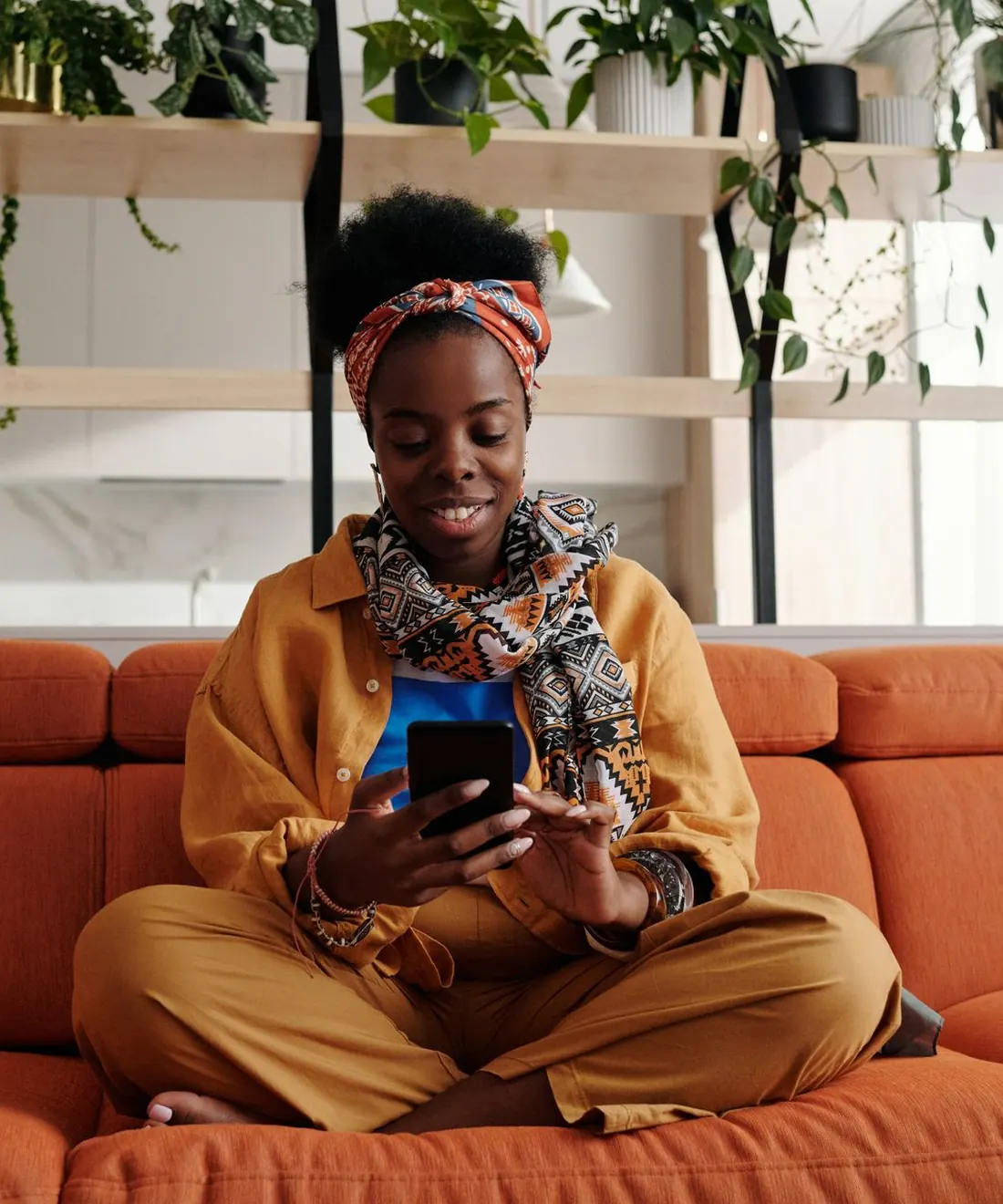 A woman in a printed headwrap shopping on her phone at home