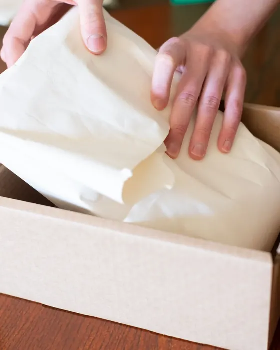 Hands wrapping an item in tissue paper inside a parcel box