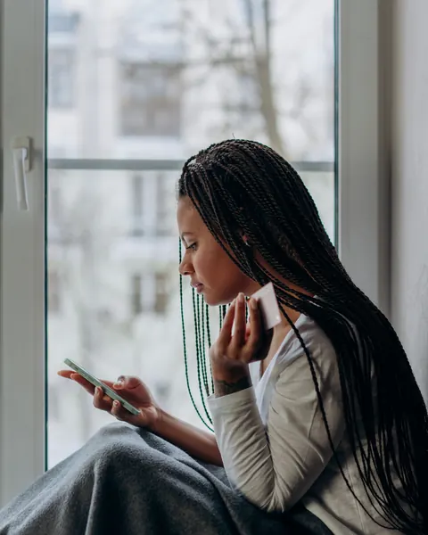 A woman by a window stares at her phone, waiting for a reply